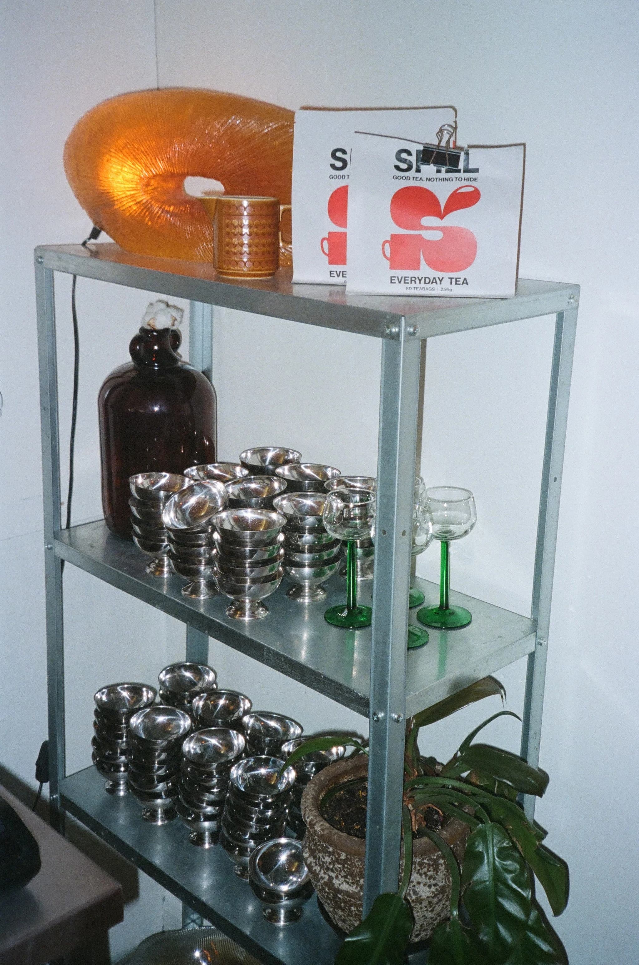 Warm shelf detail with tea boxes, glassware, and an orange lamp inside PRANA HOUSE